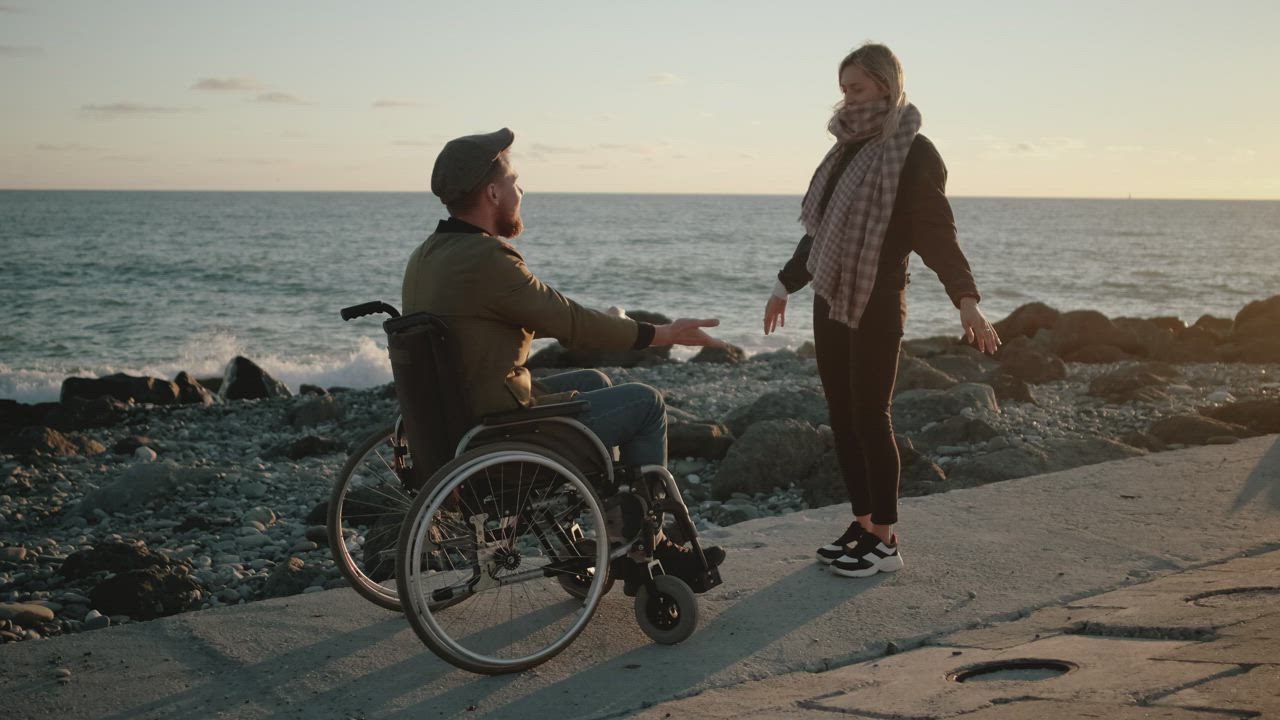 Two friends, one in wheelchair, on dock at sunset